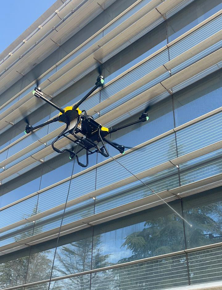 Dron industrial limpiando la fachada de vidrio de un edificio en altura
